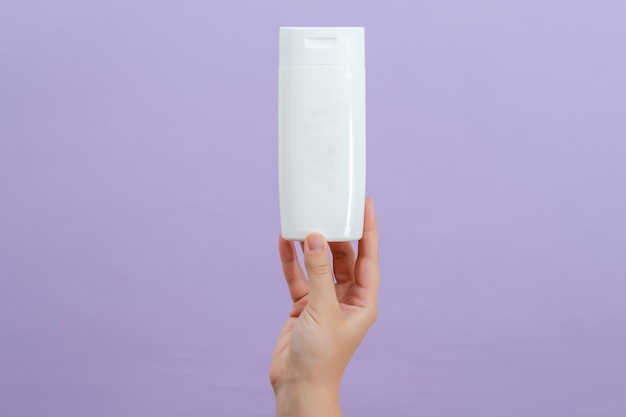 Cosmetic packaging tube in womans hand on lilac background Beauty concept Tube for cosmetic products