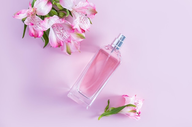 Cosmetic perfume product spray in a glass bottle on a pink background with spring flowers top view natural product