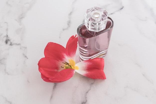 Cosmetic perfume spray or eau de toilette in a glass transparent bottle on a marble white background and petals of a spring flower space for text