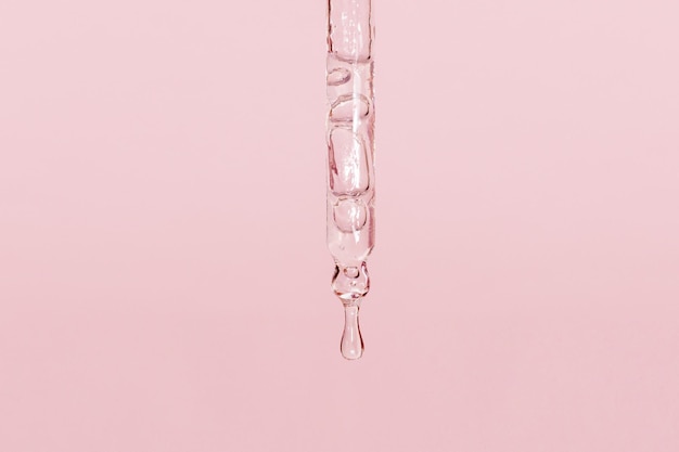 Pipetta cosmetica con liquido gocciolante e gocce su sfondo rosa siero siero gel vitamina acqua olio