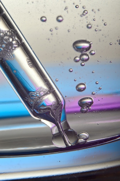 Cosmetic pipette with drops of transparent liquid and a jar, close-up on a colored background.