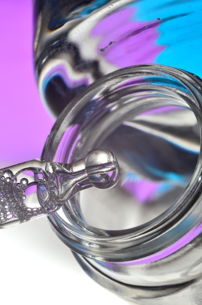 Cosmetic pipette with drops of transparent liquid and a jar, close-up on a colored background.