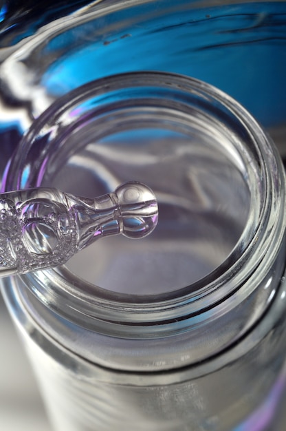 Cosmetic pipette with drops of transparent liquid and a jar, close-up on a colored background.