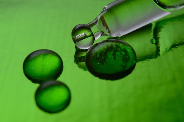 a cosmetic pipette with liquid lies on a green background covered with drops. close-up.