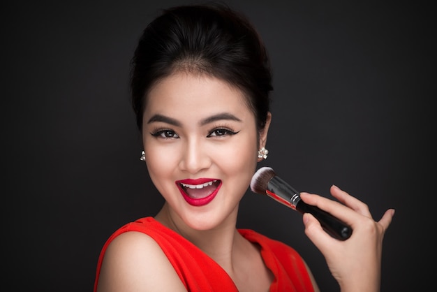 Cosmetic powder brush. Asian woman applying blusher on her cheeks with perfect make-up and red lips