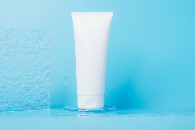 Cosmetic product in tube splashes and drops of water on blue background Shampoo gel balm white packaging
