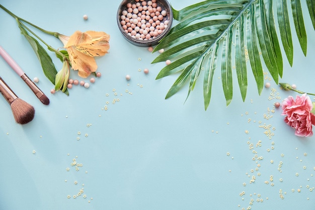 Prodotti cosmetici accessori pennelli per trucco e cipria decorazioni floreali concetto di bellezza vista dall'alto spazio copia sfondo blu foto di alta qualità