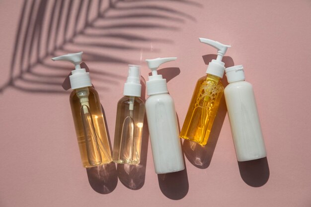 Cosmetic products in bottles on a pink background with tropical palm leaf shadow