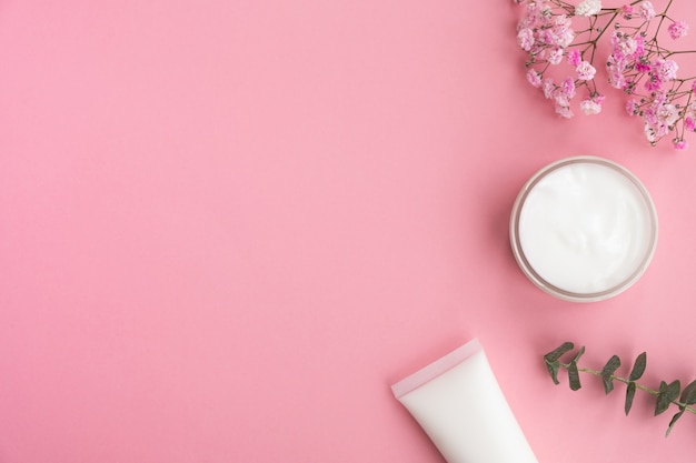 Cosmetic products, flowers and eucalyptus leaves on pink.