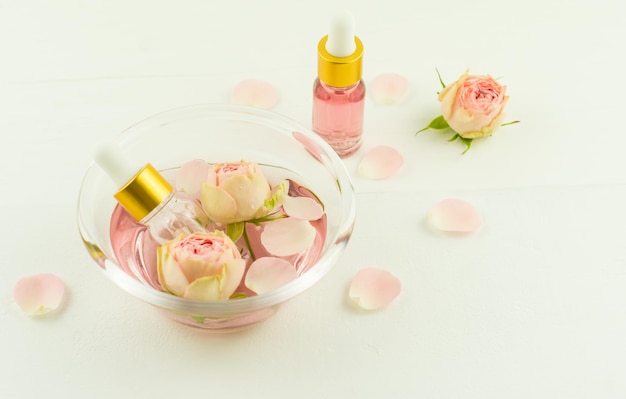 Cosmetic rose oil in bottles with a pipette in a glass bowl on a white wooden table. the concept of natural self-care.