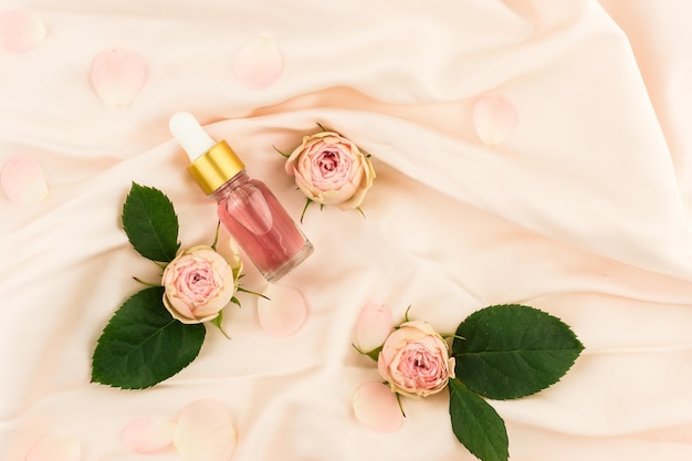 Cosmetic rose oil or essential oil in a bottle dropper on a pink textile background with rose buds and leaves. the concept of natural cosmetics.