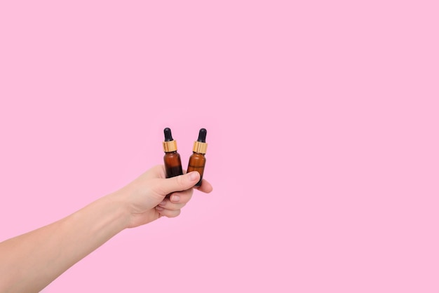 Cosmetic serum in transparent glass dropper bottles on a pink background in a woman's hand. the concept of natural skin care products. Essence skin care products for beautiful healthy skin.