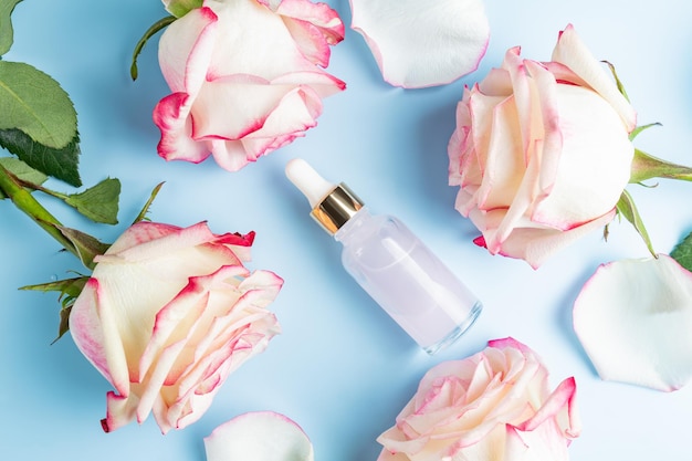 Cosmetic serum with essential rose oil and roses on a blue background A natural product for detoxifying moisturizing toning and regenerating the skin Unbranded product mockup