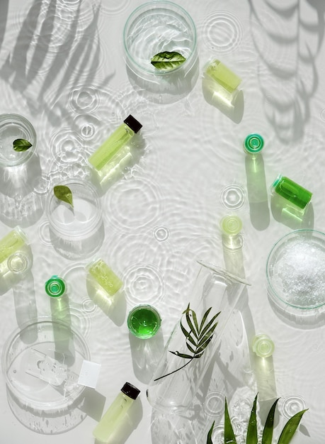 Cosmetic skincare background. Herbal medicine with green leaves. Natural sunlight, long shadows. Splashes of water, splashes. Chemical glassware, petri dishes, vials. Natural body care concept.