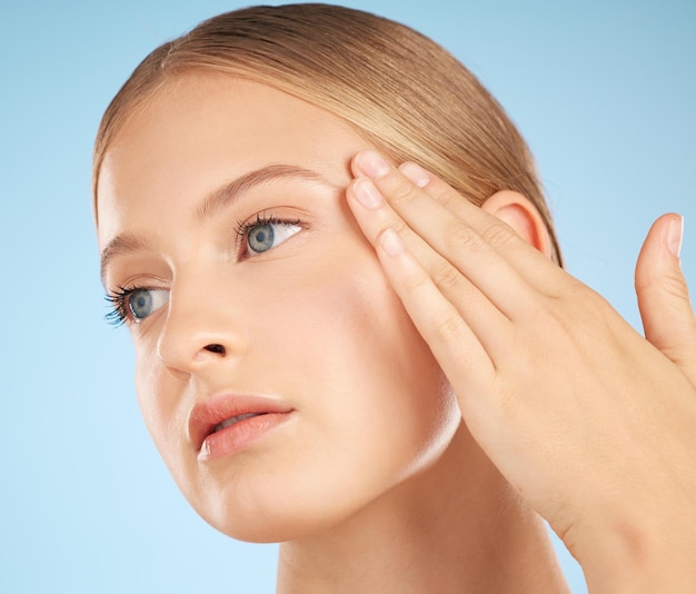 Cosmetic skincare face of beautiful woman on blue background in studio and side profile with hand on temple Young blonde model with clean finger nails luxury beauty product and natural makeup