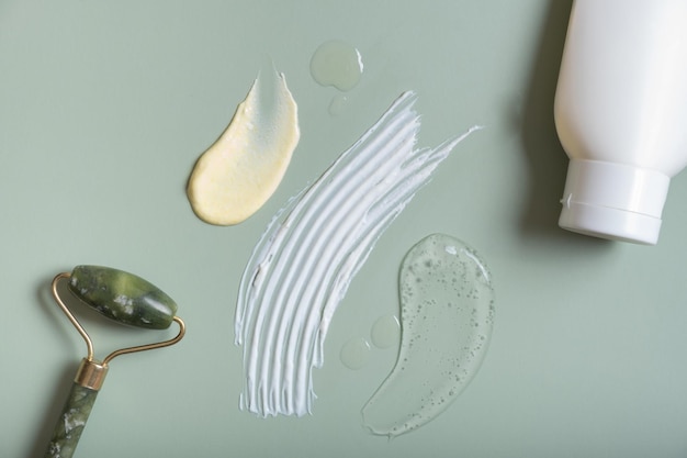 Cosmetic smears and bottle with roller on colored background\
top view on pastel green background