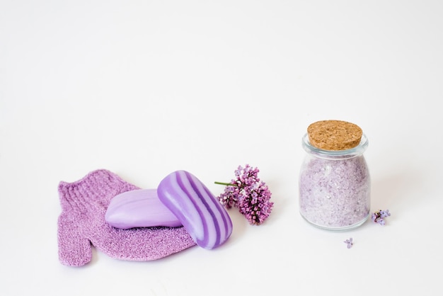 Cosmetic spa set for body care Sea salt in a glass jar organic soap washcloth mitten and lilac flowers on a light background