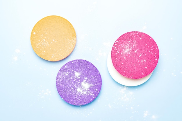 Cosmetic sponges and powdered transparent matte powder on a blue background The concept of makeup face cosmetics skin care Minimalism top view