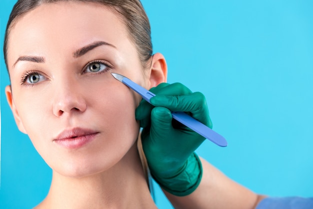 Cosmetic surgeon examining female client in office. Doctor checking woman's face, the eyelid before plastic surgery, blepharoplasty. Surgeon or beautician hands touching woman face