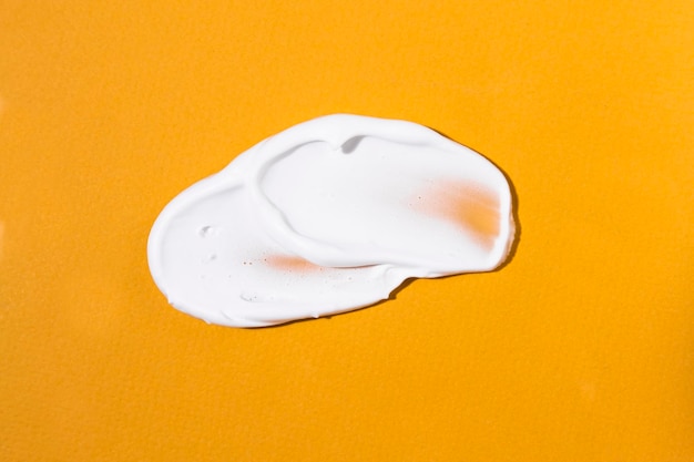 Cosmetic texture of white cream on a bright yellow background top view Beauty product for skin care