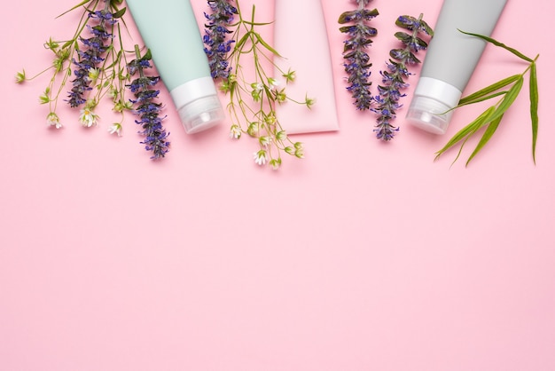 Cosmetic tubes on pink background with wild flowers and plants