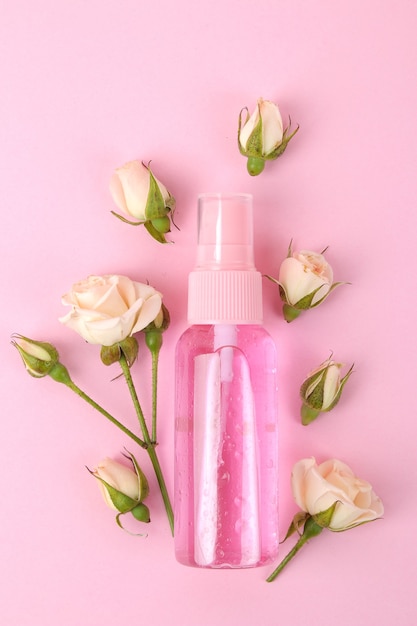 Cosmetica voor gezicht en lichaam in roze flessen met verse rozen op een delicate roze achtergrond. uitzicht van boven.