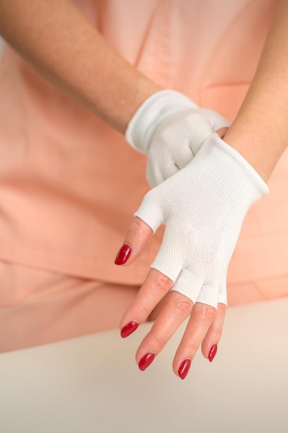 ビューティーサロンで彼女の手に白い竹の指なし手袋を着用している作業服の化粧品。
