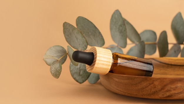 Cosmetics bottle from brown glass laying on the wooden plate with eucalyptus branch behind