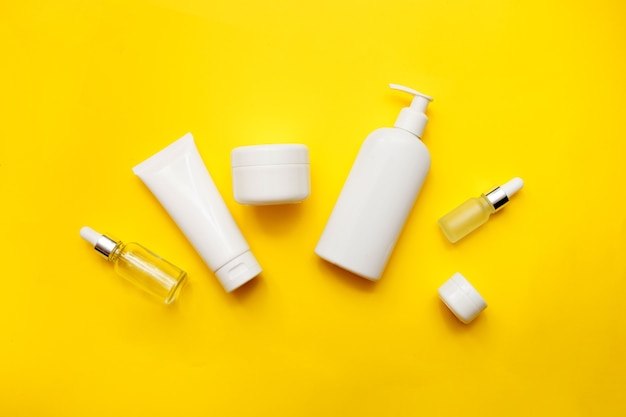 Cosmetics bottles on bright yellow background, top view, copy space. Mock up. White jars, bath accessories. Face and body care concept.