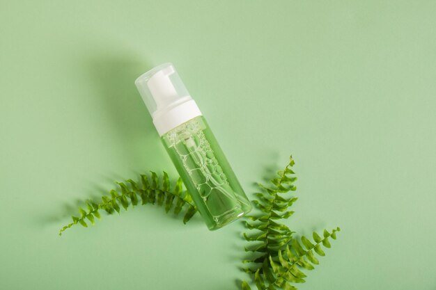 Бутылки с косметикой и свежие листья папоротника на зеленом фоне Органическая косметика Косметика СПА брендинг макет