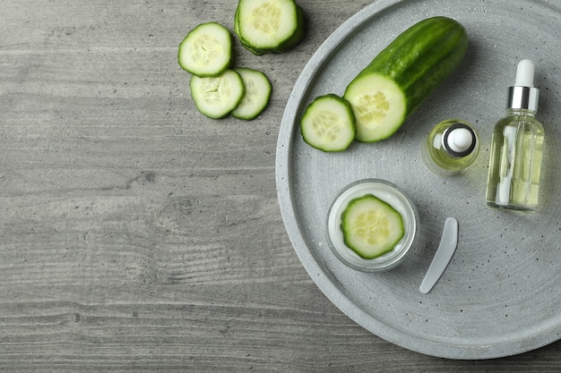 Cosmetics and cucumber on tray on gray textured