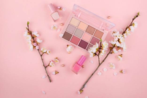 Cosmetics and flowers on a pink background with space for text