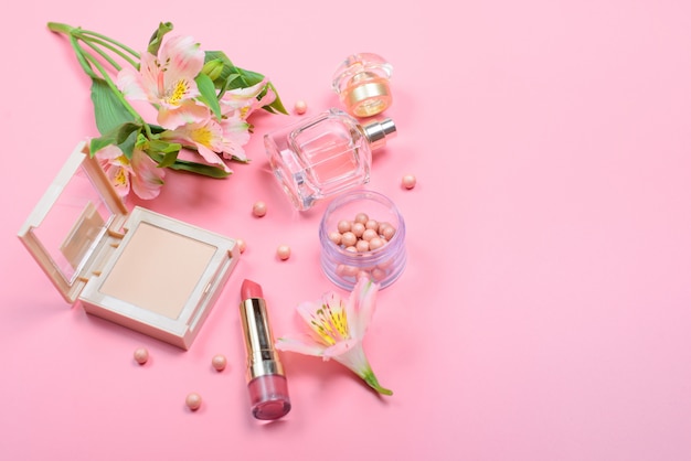 Cosmetici e fiori su una tavola rosa con copyspace