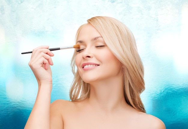 cosmetics, health and beauty concept - beautiful woman with closed eyes and makeup brush