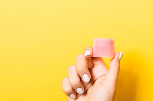 Cosmetics jar in female hand over yellow background