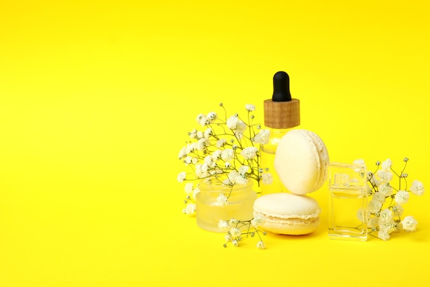 Cosmetics, macaroons and flowers on yellow background