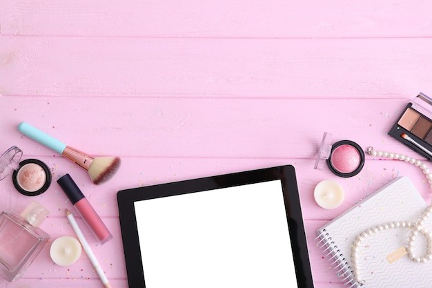 Cosmetics and modern tablet on a colored background top view