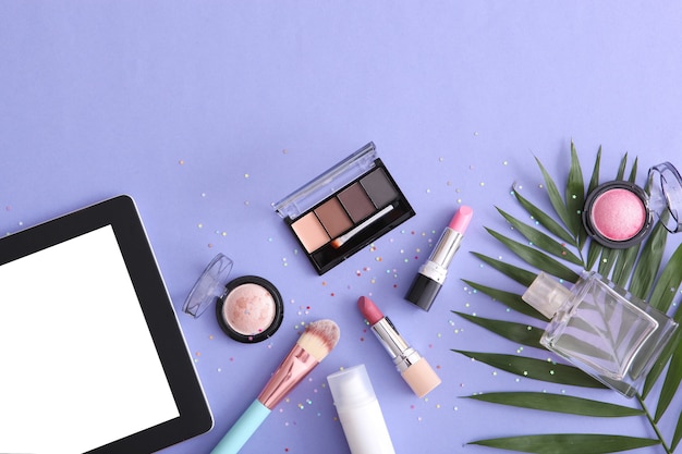 Cosmetics and modern tablet on a colored background top view