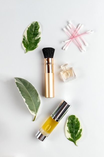 Cosmetics and selfcare A composition of green leaves brush cotton sticks perfume and oil in a tube are laid out on a white background Flat lay Vertical