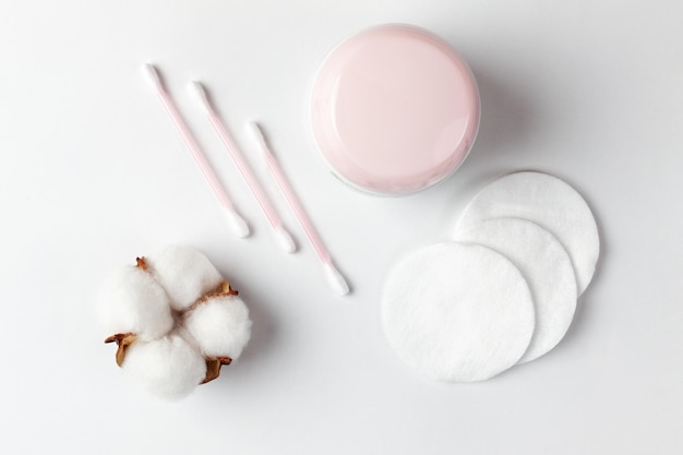 Cosmetics and selfcare On a white background cotton pads cotton sticks a cotton flower and a jar of cream are beautifully laid out Flat lay