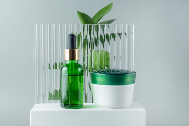 Cosmetics SPA branding mockup Green glass cosmetic bottles and jars on on white podium on gray background with copy space Natural organic beauty product concept Minimalism style