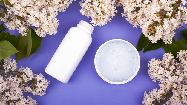 Cosmetics in white bottles on a purple background with branches of white lilac top view, skin care, beauty, cleansing and moisturizing body