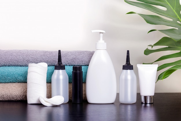 Cosmetics in white tubes and bath products on a black table with tropical leaves.