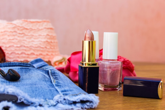 Cosmetics and women's accessories: lip gloss, nail polish, hat, denim shorts and headphones on table 