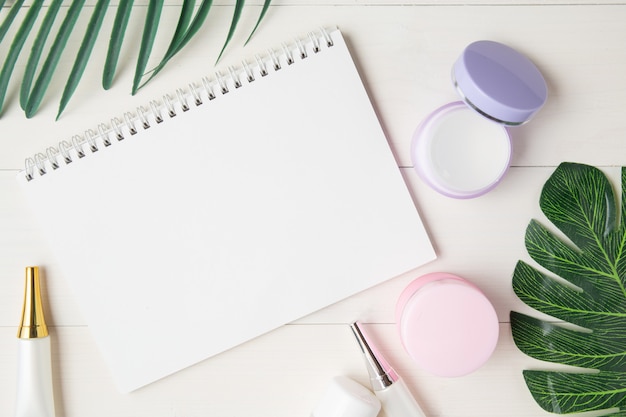 Cosmetisch en huidverzorgingsproduct en notitieboekje en bladeren op tafel