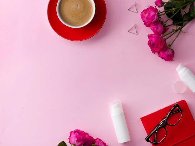 Cosmetisch huidverzorgingsproduct, notebook, koffie en bloemen op roze