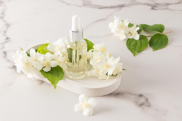 Cosmetisch product met essentiële jasmijnolie in een glazen fles met een druppelaar op een wit gipsen dienblad met verse bloemen van de plant