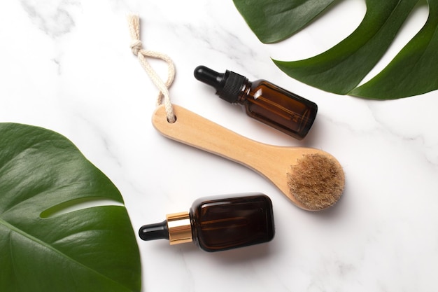 Cosmetisch serum in bruine glazen fles en lichaamsborstel op een marmeren achtergrond met monstera palmblad