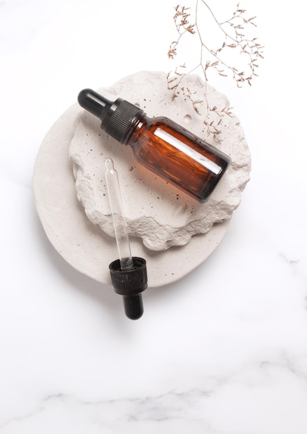 Foto cosmetisch serum in glazen fles op stenen podium natuurlijk cosmetisch product verpakkingsontwerp branding marmeren achtergrond met bloementak