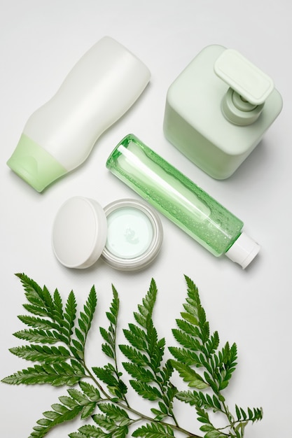 Cosmetische containers met groene kruidenbladeren, blanco labelpakket voor branding. Hydraterende crème, shampoo, tonic, huidverzorging voor gezicht en lichaam.